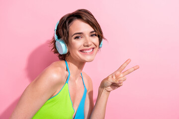 Fototapeta premium Photo of pretty good mood lady wear green blue tank top listening music headphones showing v-sings isolated pink color background