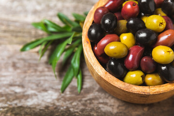 Green, black and red olives, olive oil on a brown wooden background. Fresh juicy olives in a bowl and fresh olive leaves. Vegan. Olive fruits. Place for text. Copy space.
