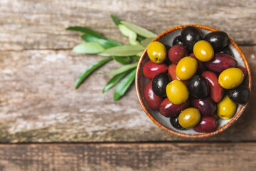 Green, black and red olives, olive oil on a brown wooden background. Fresh juicy olives in a bowl and fresh olive leaves. Vegan. Olive fruits. Place for text. Copy space.