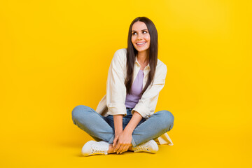 Full length photo of gorgeous positive minded person sit floor look empty space ad isolated on yellow color background
