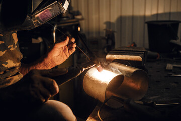 Male in face mask welds with argon welding. Industrial welder worker welding using argon machine, close up. Man working with arc welding machine in garage. - obrazy, fototapety, plakaty