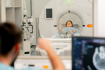 A girl lies on an MRI machine before examining her body and the radiologist gives command to her to...