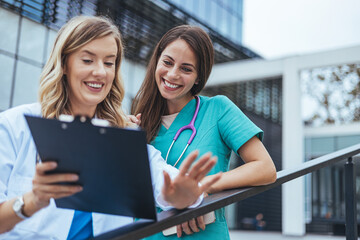Shot of two nurses having a discussion in a hospital. Close up of a two cheerful smiling professional female doctors with stethoscope looking at the clipboard of a patient.
