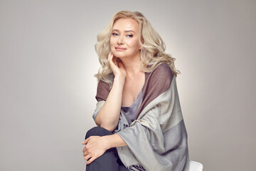 Fototapeta premium Mature older woman wearing in tippet plaid sitting on chair over grey isolated.