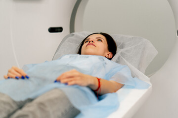 A girl in a medical gown lies on a movable couch of a magnetic resonance imaging machine and...