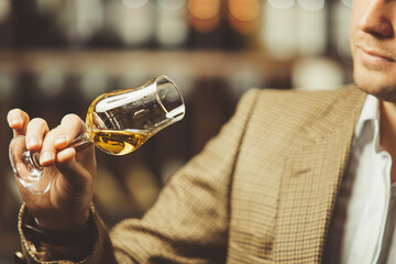 Sommelier holding a glass of whiskey, evaluates the color, smell and taste of alcoholic beverage.