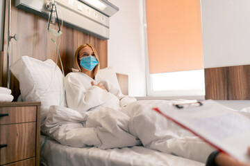 A girl in a hospital room in a medical mask in quarantine describes to doctor complaints about her...