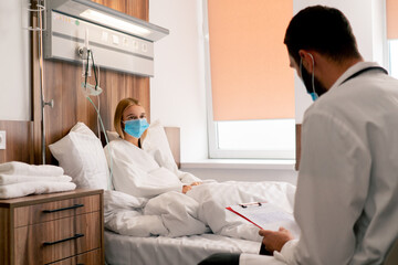 A girl in a hospital room in a medical mask in quarantine describes to doctor complaints about her...