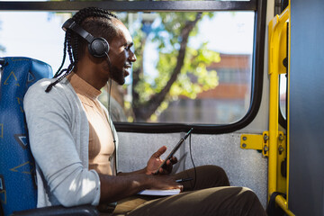 Young black man, wearing headphones, listening to music on his smartphone, during bus ride.