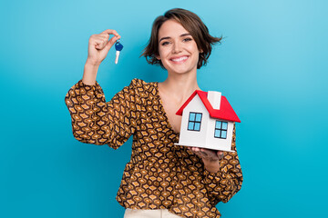 Photo of pretty cheerful girl toothy smile hands hold showing little house key isolated on blue...