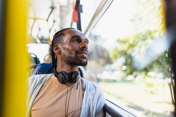 Young black man, with headphones, looking out the bus window.