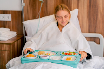 A girl lying in a hospital room is brought tray with delicious food to strengthen her strength and recover from illness