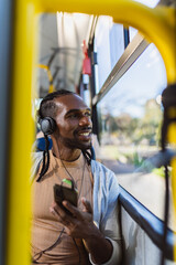 Jovem negro sorridente, usando fones de ouvido, ouvindo musica em seu smartphone.