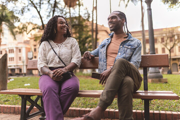 Cheerful young friends talking while sitting on the bench in the square on a sunny afternoon.