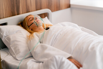 Close-up shot of a girl lying in hospital room wearing an oxygen mask to maintain breathing during...