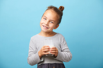 Funny child girl with glass of milk, stands over blue background.