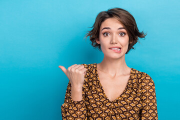 Photo of pretty nervous person biting lips indicate thumb finger empty space isolated on blue color background