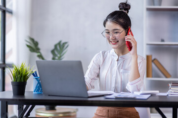 Cheerful Young business Asian woman freelancer making telephone call share good news about project working in office workplace, business finance concept.	
