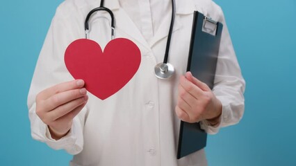 Close up of unknown woman doctor in uniform with stethoscope holding red heart shape, isolated over blue background. Love, donor, world heart day, world health day, CSR donation and Insurance concept