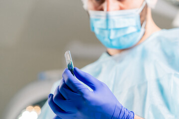 Close-up shot of a surgeon in a protective headdress and a medical mask holding scalpel in his hands and looking at it carefully