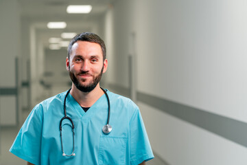 Portrait of a smiling doctor with a beard and a stethoscope around his neck in the corridor of...