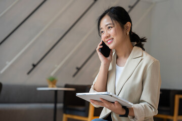 Freelance Asian woman working online at coffee shop, woman talking with customer with mobile phone