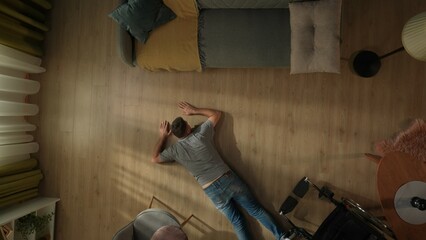 A disabled man lies on the living room floor after falling from his wheelchair. Top view of a helpless man lying face down on the floor. © kinomaster