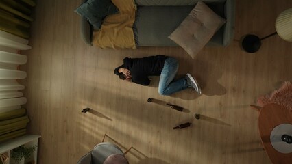 Top view of a man lying on the floor next to empty beer bottles. Drunk man holding his head,...