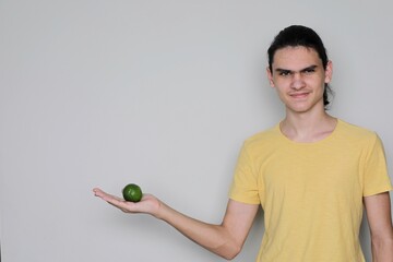 Young man holds lime in his palm and expresses distrust and disdain with his face. Concept of food doubt, subject