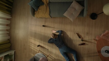 Top view of a drunk woman crawling across the living room floor. Woman on the floor surrounded by beer bottles. Alcoholism. Hopelessness. Alcohol addiction treatment.