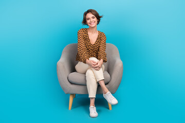 Full body photo of cheerful pretty lady sit comfy soft chair crossed legs good mood isolated on...