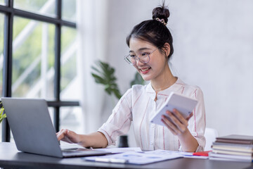 Young Asian Business woman Using laptop computer and working at office with calculator document on...