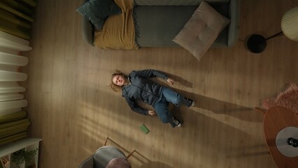 Top view of a young woman lying on the living room floor next to a smartphone. The woman is...