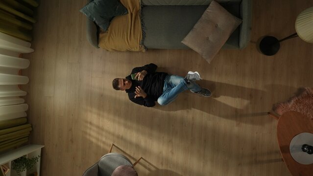 Top view of a shocked man lying on the living room floor with a smartphone in his hands. Gadget addiction.