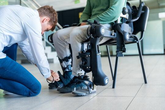 Mechanical exoskeleton. Physiotherapy in a modern hospital: Physiotherapist placing the tapes on the knees of the disabled person to place his robotic skeleton
