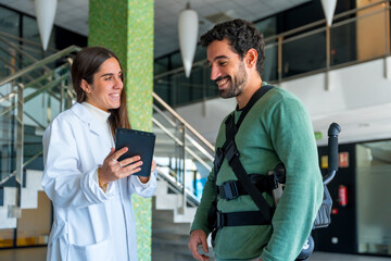 Mechanical exoskeleton, female physiotherapist doctor talking with tablet with disabled person with...