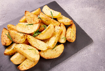 Baked potato wedges with seasonings on a stone tray on a gray st