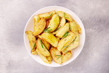 Baked potato wedges with seasonings on a plate on a gray stone.