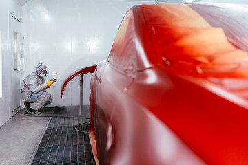 Professional male car mechanic working with spray gun painting part of auto body in automotive paint service shop. Automobile painter painting car in chamber. - obrazy, fototapety, plakaty