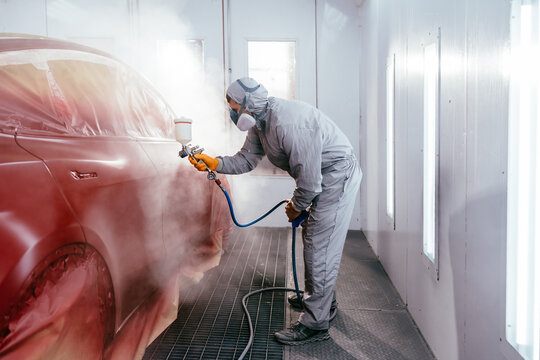 Automotive paint services, quality auto body shop concept. Repairman painter in chamber painting automobile car.