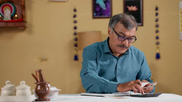 Indian senior man with eye glasses splitting monthly bills by calculating at home - concept of budget planning, retirement lifestyles and financial responsibility or spending