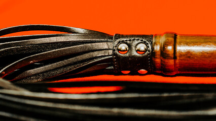 bdsm attribute black leather lash on a red background close-up