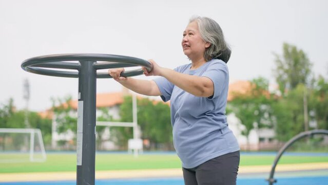 Senior Asian woman in casual workout in exercise stations in public park. Represents keeping young with physical activity, Open air gym. Physical health concept. Outdoor fitness equipment in city park