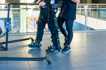 Mechanical exoskeleton. Female physiotherapy doctor helping unrecognizable disabled person with robotic skeleton to walk. Futuristic rehabilitation, Physiotherapy in a modern hospital