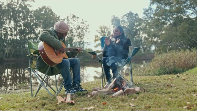 Camping, fire and music with a guitar couple in nature, bonding together in the wilderness for romance or dating. Hiking, travel or instrument with a man musician and woman by a lake in the forest