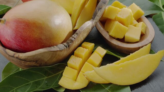 Ripe mango fruits with slices and mango leaves slowly move in the frame on a gray stone table. Nice fruit background for your projects. Macro video shooting.
