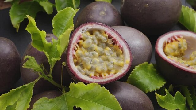 Ripe passion fruits with passion fruit seeds and passionfruit leaves slowly move in the frame on a gray stone table. Nice exotic fruit background for your projects. Macro video shooting.
