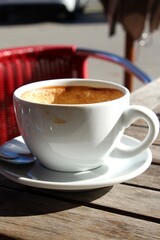 Eine Tasse Cappuccino in einem Café auf der Terrasse an einem sonnigen Oktobertag. Roter Stuhl im Hintergrund.

Allgäu, Bayern