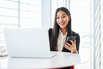 Smiling businesswoman working at office using laptop and smartphone for 2FA