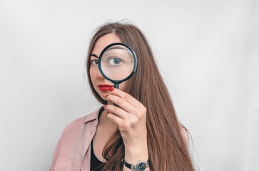 Close up of young brunette woman looking through magnifying glass, isolated over white background